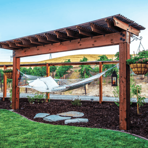 Wood shade arbor with a hammock between two posts.
