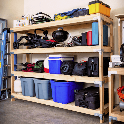 Storage containers, suitcases, grill, and coolers sitting on a wood garage shelf.