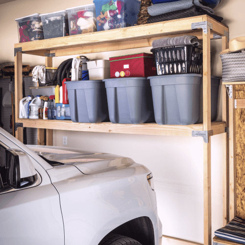 Storage containers on a shelving unit with a car partially parked under it in garage.
