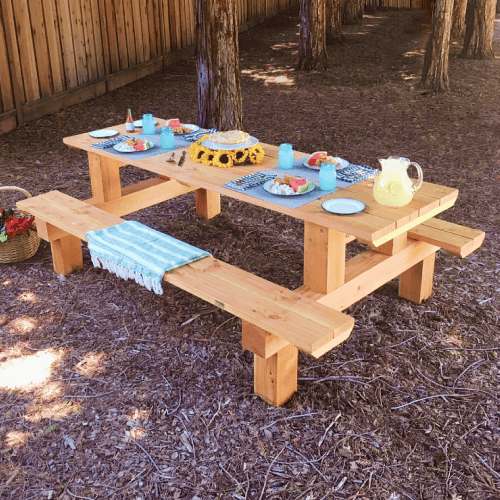 Solid wood picnic table set up for lunch in backyard.