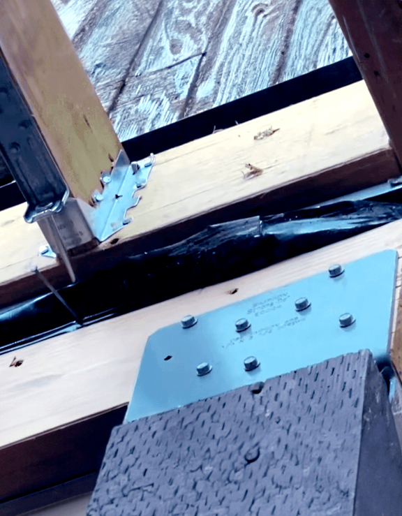 Close-up view of galvanized steel connectors securing wood framing for a deck, showing fasteners and joist hardware in use.