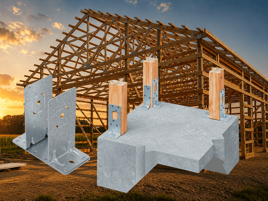 Large timber-framed building under construction at sunset, with exposed roof trusses and wood framing. In the foreground, galvanized metal post base connectors and a concrete foundation mockup with wood posts and metal brackets are displayed against the construction site background.
