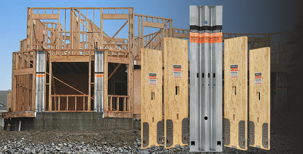 Large timber-framed building under construction at sunset, with exposed roof trusses and wood framing. In the foreground, galvanized metal post base connectors and a concrete foundation mockup with wood posts and metal brackets are displayed against the construction site background.