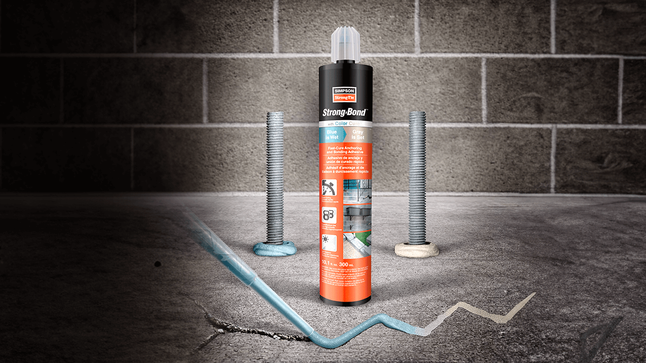 Strong-Bond adhesive tube on cracked concrete with bolts and blue adhesive line; brick wall in background.