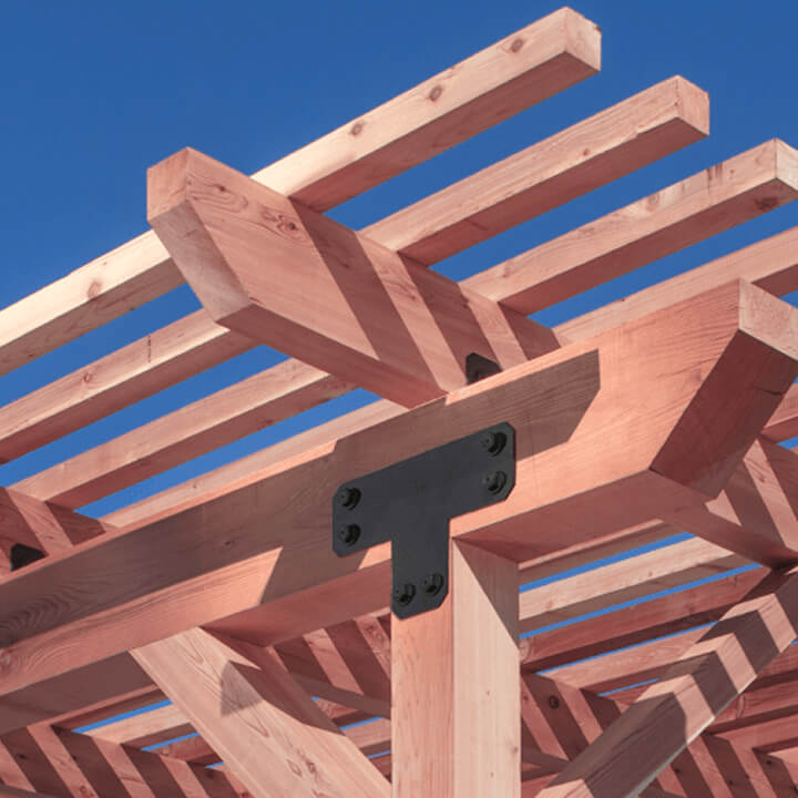 A close-up view of a wooden pergola frame with exposed beams and Outdoor Accents metal connectors set against a clear blue sky.