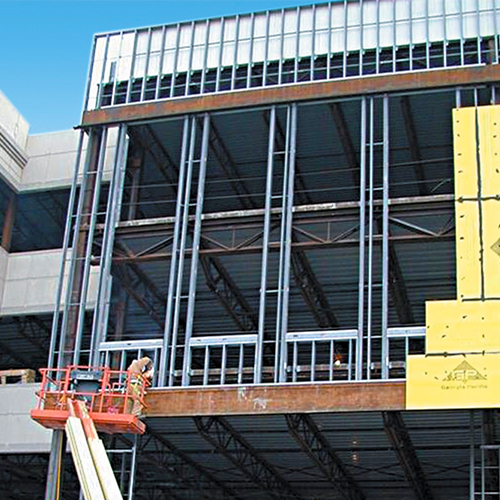 Building structure with Cold-Formed Steel framing products on one side of it's exterior. Construction worker on a orange crane construction vehicle is working on the bottom part of the CFS frames.