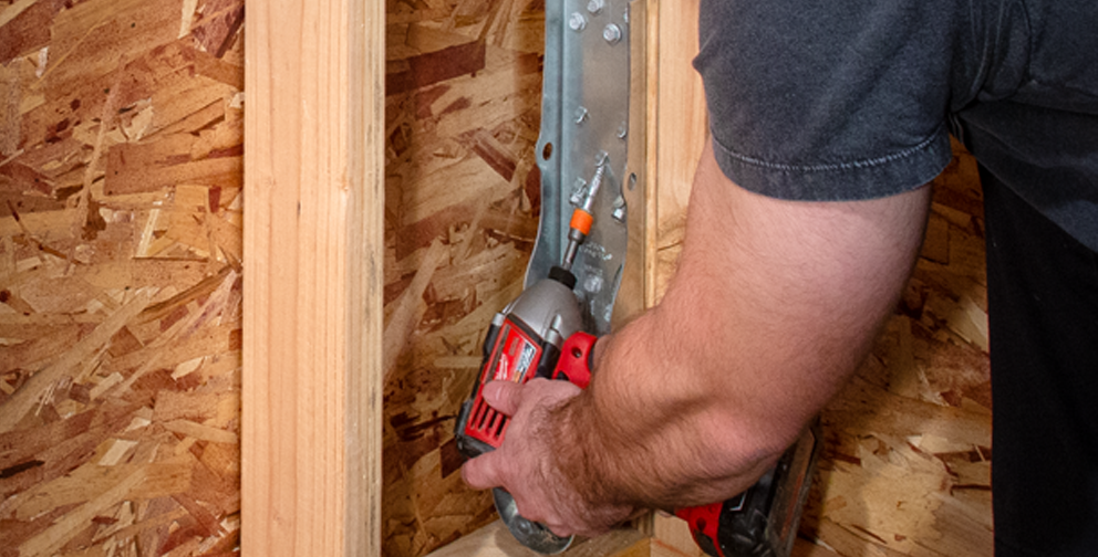 Man using red drill gun to install HDUE7 product into wooden panel.
