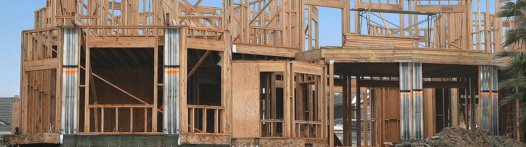 Wood-framed residential structure under construction with elevated foundation supports, exposed wall framing, and building materials visible in the foreground.