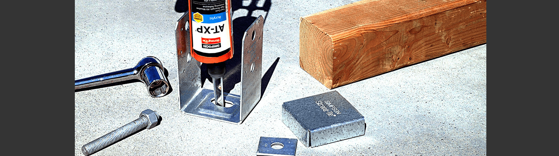 Simpson Strong-Tie AT-XP adhesive anchor system being applied to a metal base bracket, with accompanying bolt, wrench, and wooden beam.