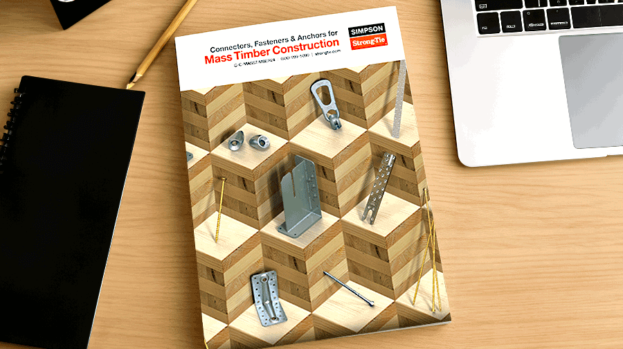 Mass Timber Construction catalog on a desk next to a notebook and laptop, featuring connectors and fasteners on a 3D wood cube cover design.