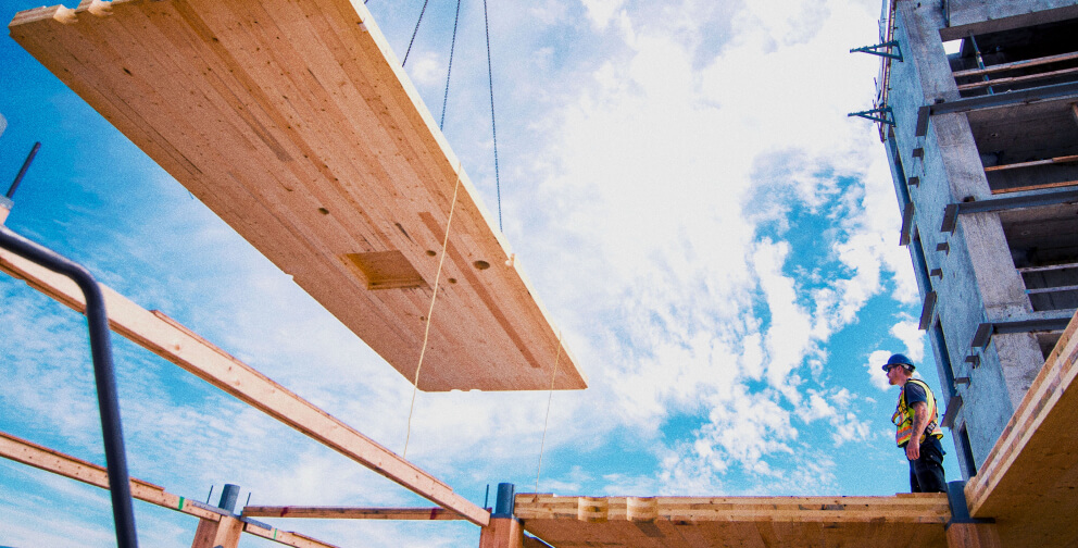 Construction working monitoring mass timber being lifted.