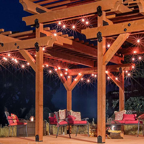 Outdoor deck with stacked pergola and iron outdoor loveseats with red pillows at night