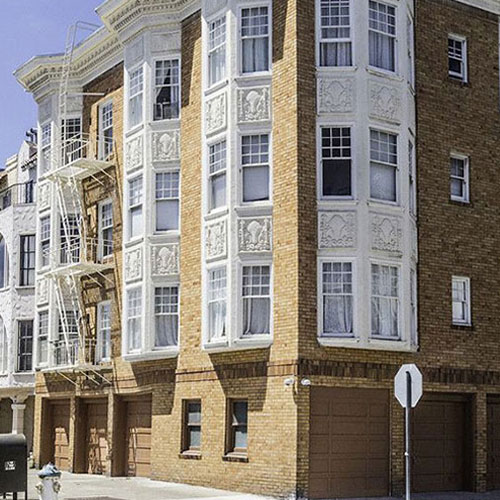 Caddy corner view of red and orange bricked building with numerous windows and white fire escape