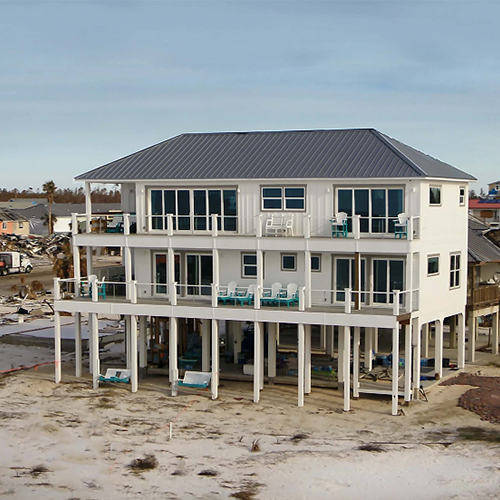 Two story white house on stilts in storm devastated neighborhood