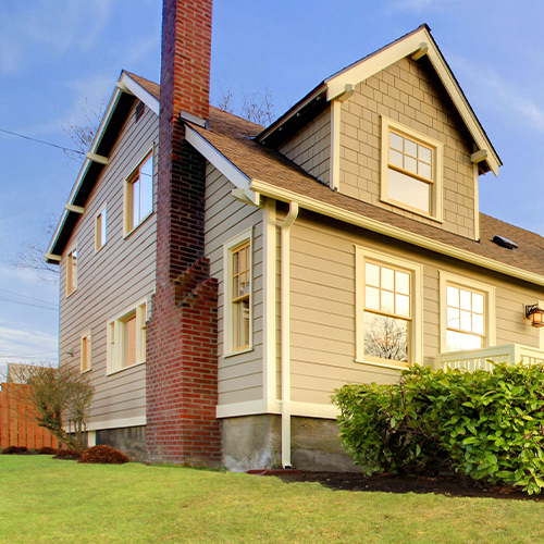 Beige wood paneled house with raised concrete foundation and grass yard.