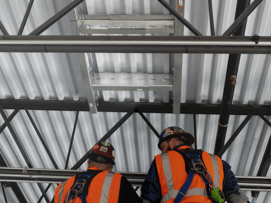 Construction workers install a QuickFrames™ support system overhead, demonstrating efficient attachment to structural steel for building services and utilities.