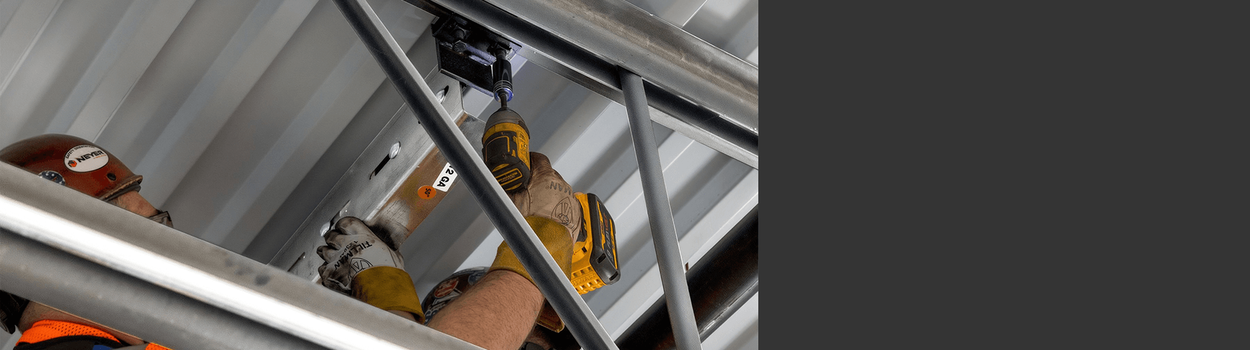 Installer secures a QuickFrames™ modular support system to structural steel using a power tool, demonstrating efficient overhead installation for electrical, mechanical, and cable management infrastructure.