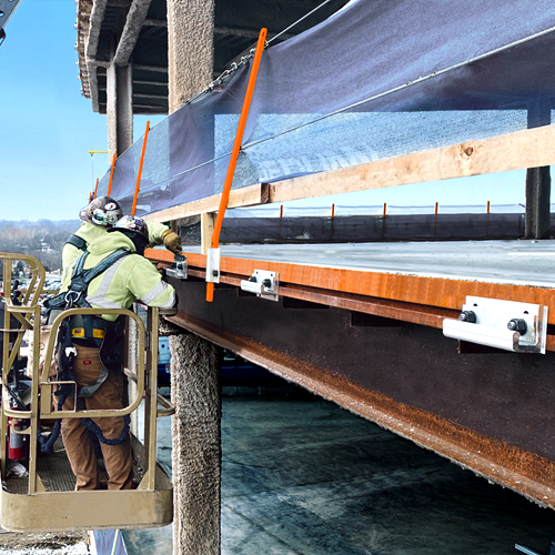 Two construction workers in safety gear securing edge tie systems to the steel structure of a building under construction. The edge tie is attached to the perimeter of the steel frame for safety and stability during construction.