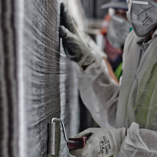 Close-up of a worker using a roller to apply fiber-reinforced polymer (FRP) to a surface for structural strengthening, wearing protective gloves.